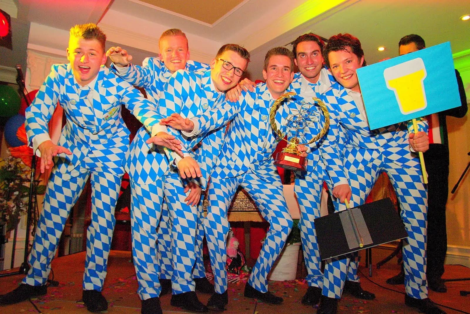 Six men in blue and white suits with a trophy on the stage of a carnival song contest in Helmond