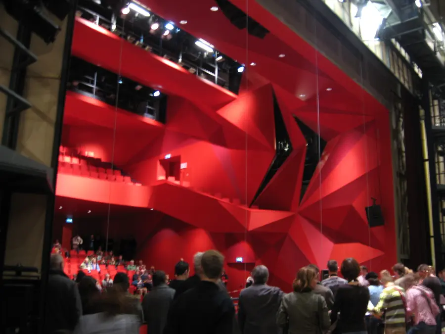 The warm-red Grote Zaal of AGORA Theater Lelystad, with rows of fixed seats facing the stage.