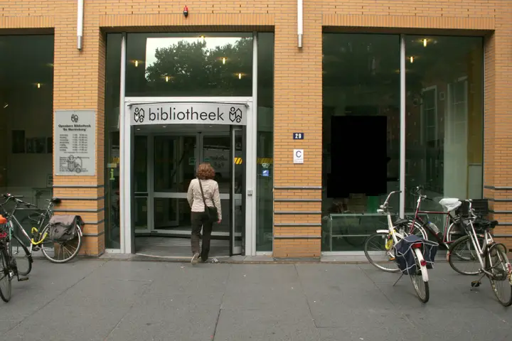 The entrance of Bibliotheek De Mariënburg in Nijmegen, with revolving doors and bicycles parked outside.