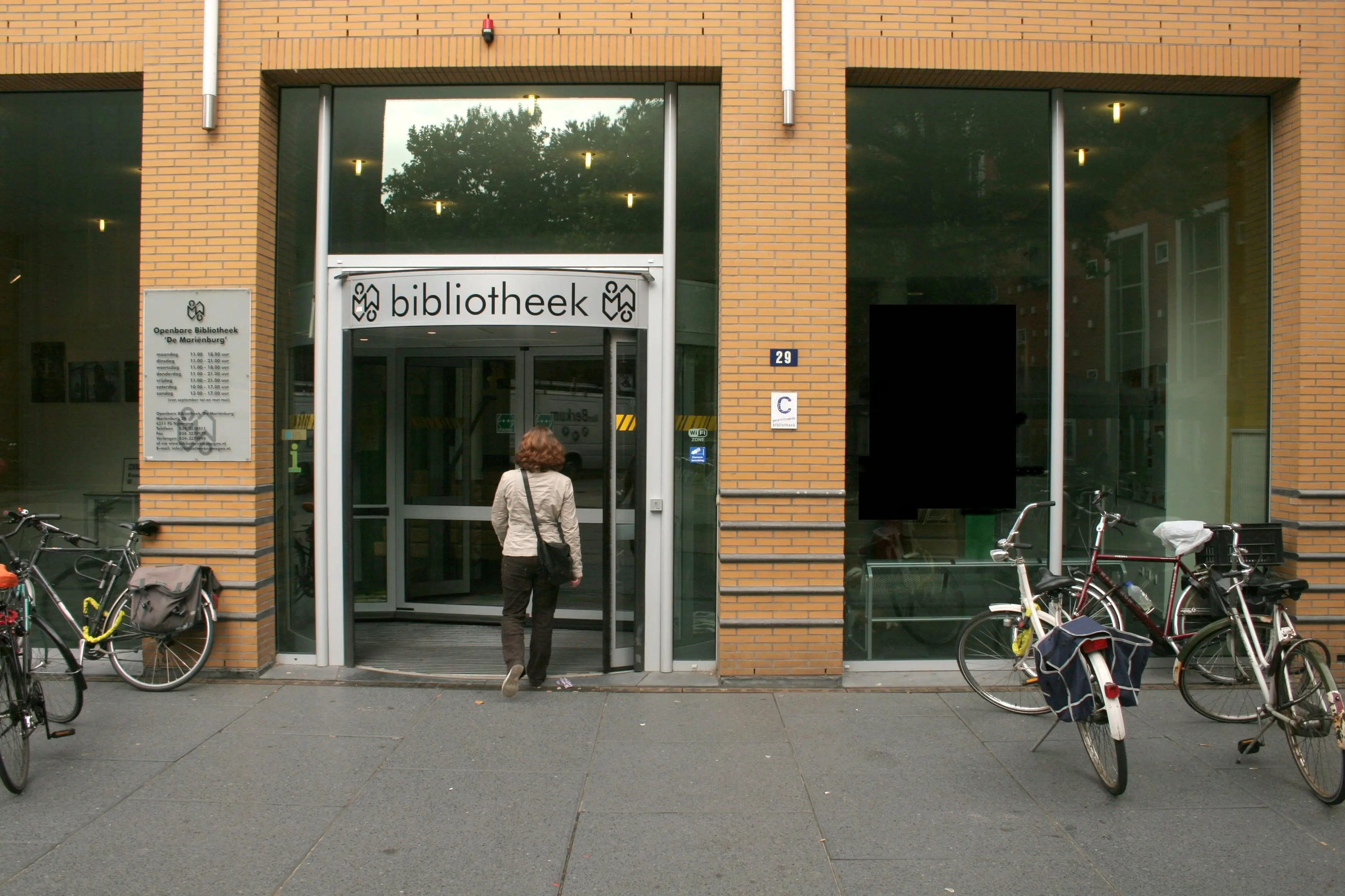 The entrance of Bibliotheek De Mariënburg in Nijmegen, with revolving doors and bicycles parked outside.