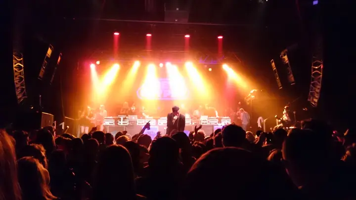 The First Avenue Main Room full of people during a show, stage lights glowing behind the crowd and speaker arrays flanking the stage