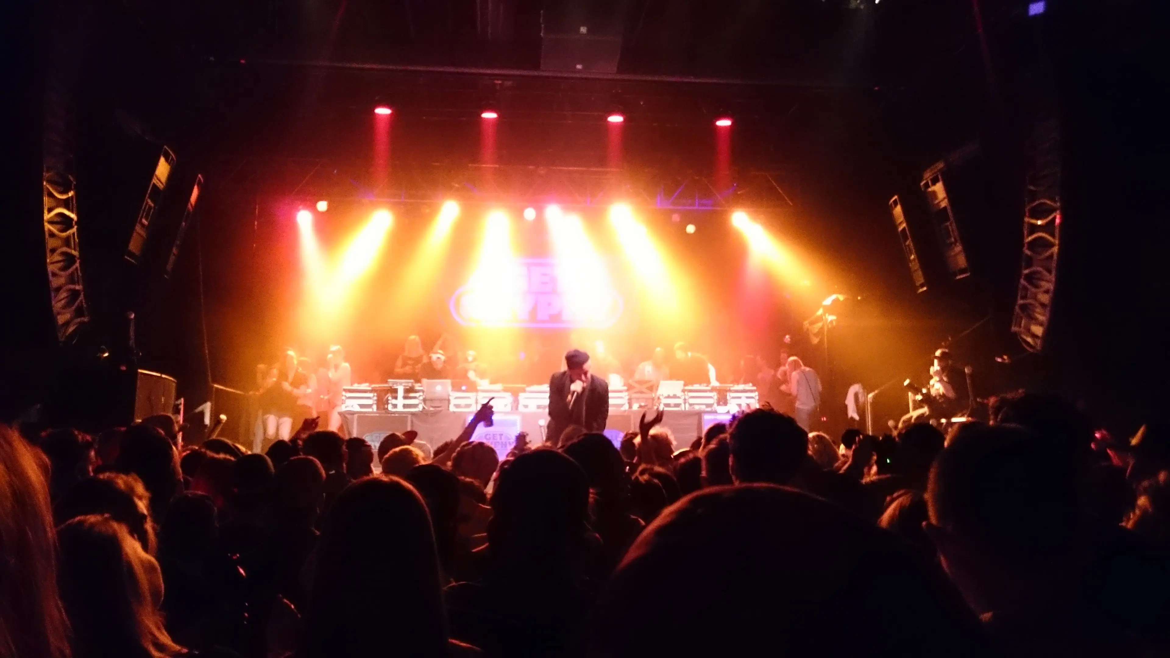 The First Avenue Main Room full of people during a show, stage lights glowing behind the crowd and speaker arrays flanking the stage