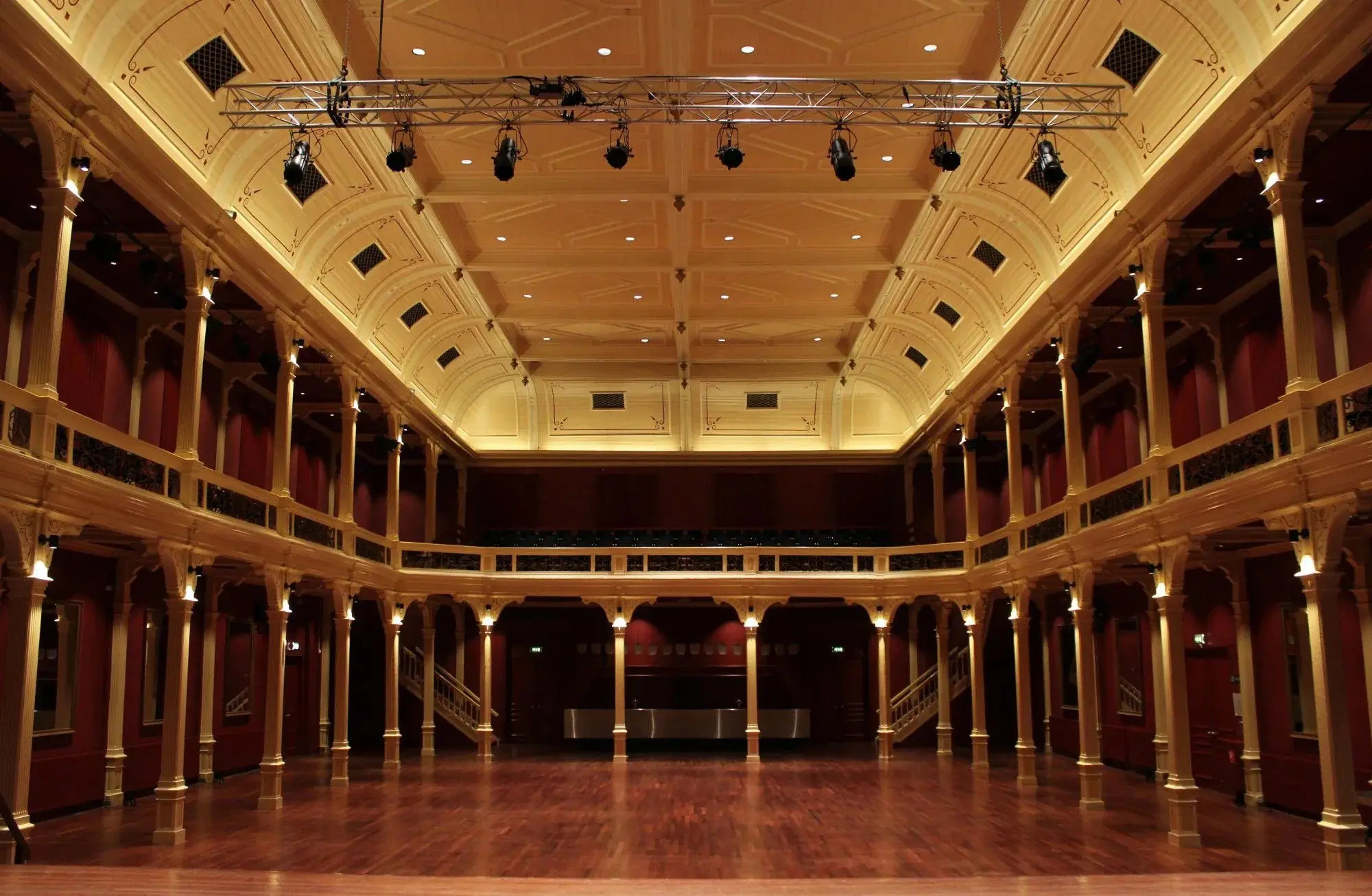 The empty Buitensociëteit concert hall of 1891, with its gallery of slender columns, wooden floor and lighting rig under a coffered ceiling.