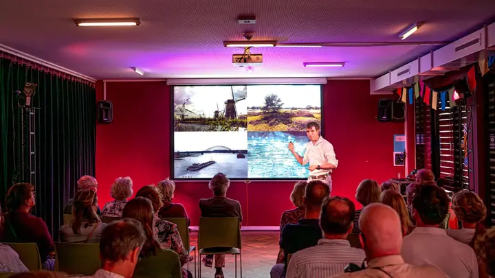 A speaker presents to an audience in Podium Hoge Woerd's Studio, with a large projection screen behind.