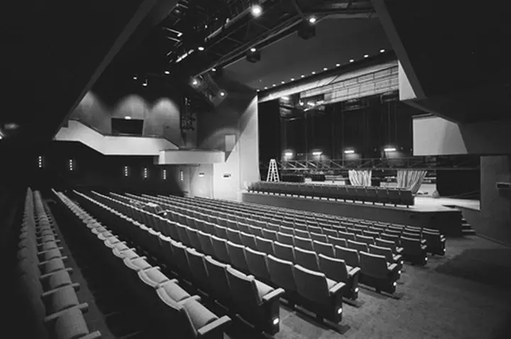 The grand hall of De Kring on the Kerkstraat in 1986, rows of empty seats facing the stage, in black and white.