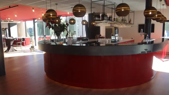 The round red bar in the foyer of Stadsschouwburg Middelburg, under hanging lamps, with the bottles and glasses behind it.