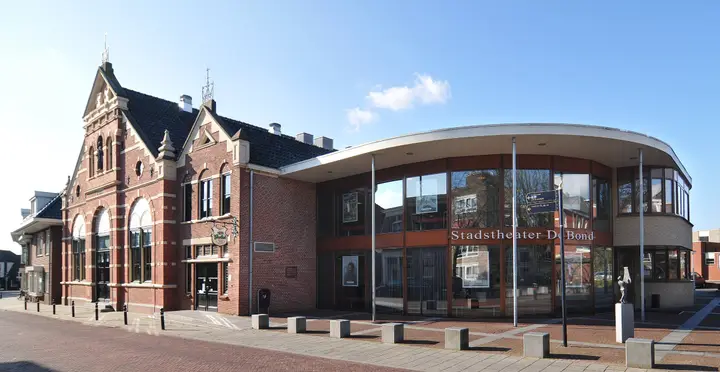 The façade of Stadstheater De Bond on Molenstraat in Oldenzaal: the older red-brick building next to the curved glass foyer, under a blue sky