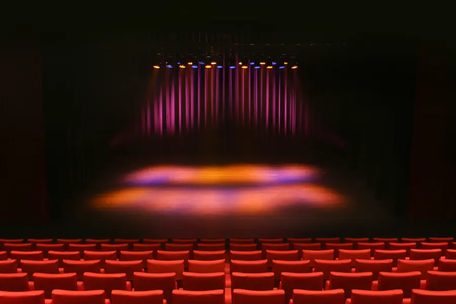 The auditorium of Stadstheater De Bond seen from the back, rows of red seats facing a stage lit in orange and purple