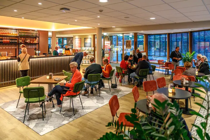 Visitors at tables in the foyer and theatre café of Stadstheater De Bond before a performance, with the bar and programme posters behind them