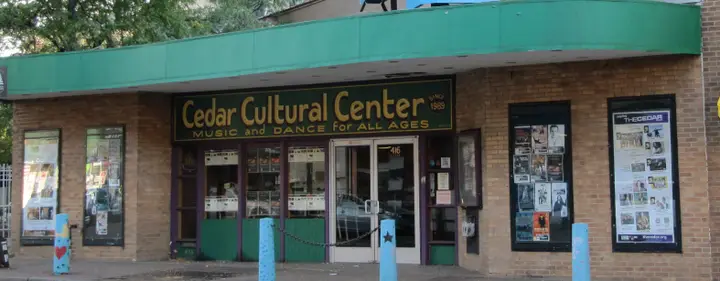 The street entrance of The Cedar Cultural Center at 416 Cedar Avenue: the painted Cedar Cultural Center sign, the glass doors and the poster cases on both sides