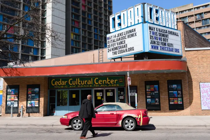 The Cedar Cultural Center on Cedar Avenue in Minneapolis by day: the tall CEDAR marquee over the former movie theater entrance, with the Cedar-Riverside towers behind