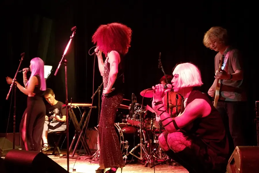 A band performing under stage lights in front of a black curtain at The Cedar Cultural Center, monitors at the lip of the stage
