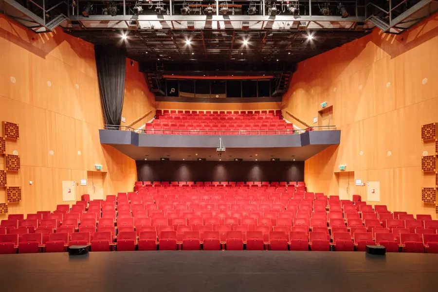 The empty theater hall of Theater de Hofnar, with red seats and a balcony, seen from the stage.