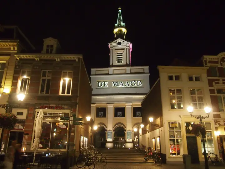 The neo-classical exterior and tower of Theater De Maagd on the Grote Markt, lit at dusk.