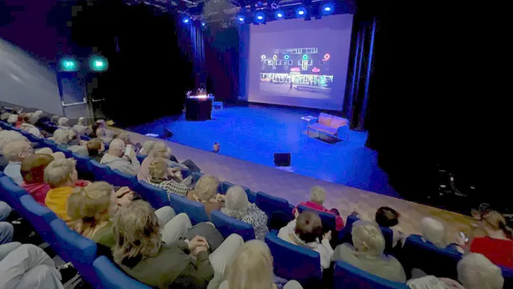The Grote Zaal of Theater De Omval with its stage lit in blue and the audience seated in the foreground