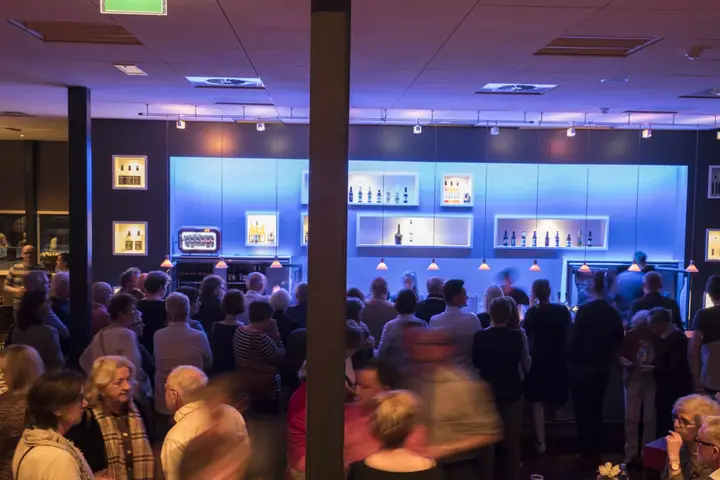 Visitors crowd the blue-lit bar in a foyer of Theater de Voorveghter, bottles on the lit shelves behind the counter.