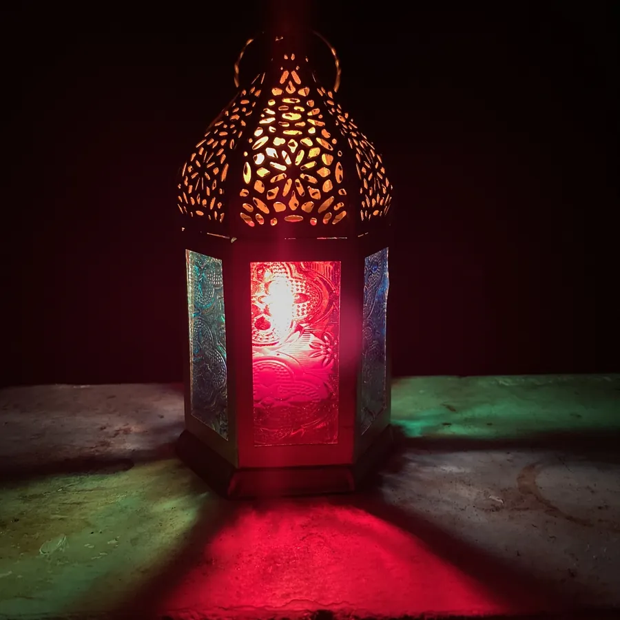 A lit Ramadan lantern of pierced metal and coloured glass in the dark, throwing green and red light
