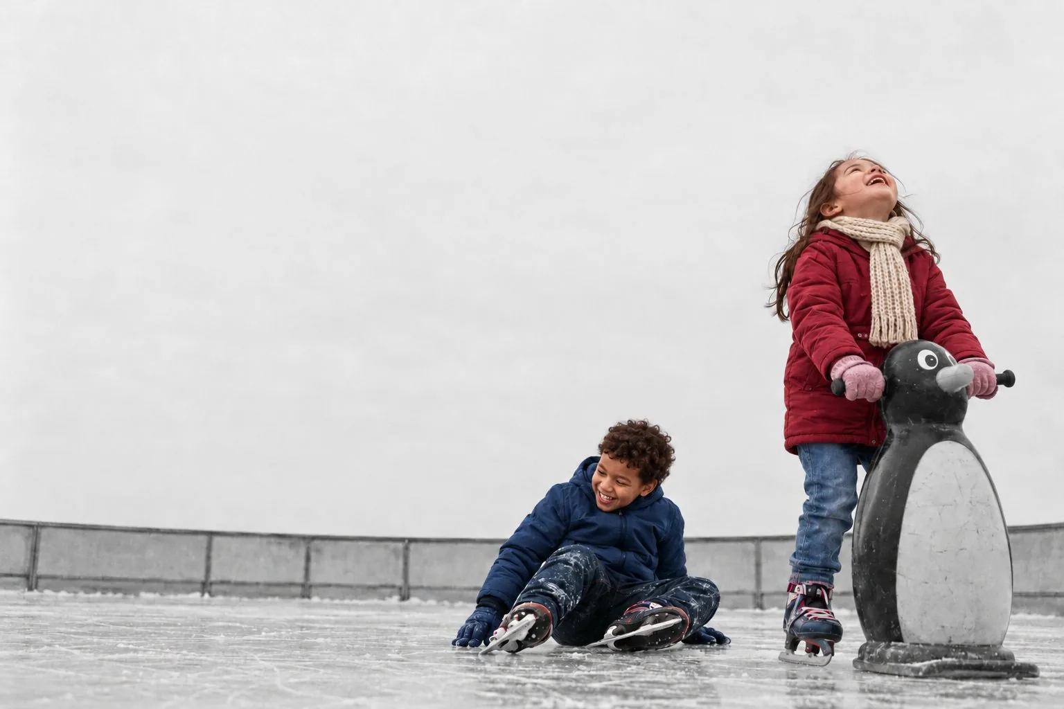 AI image: a girl on an ice rink looks up laughing, a boy who just fell laughs